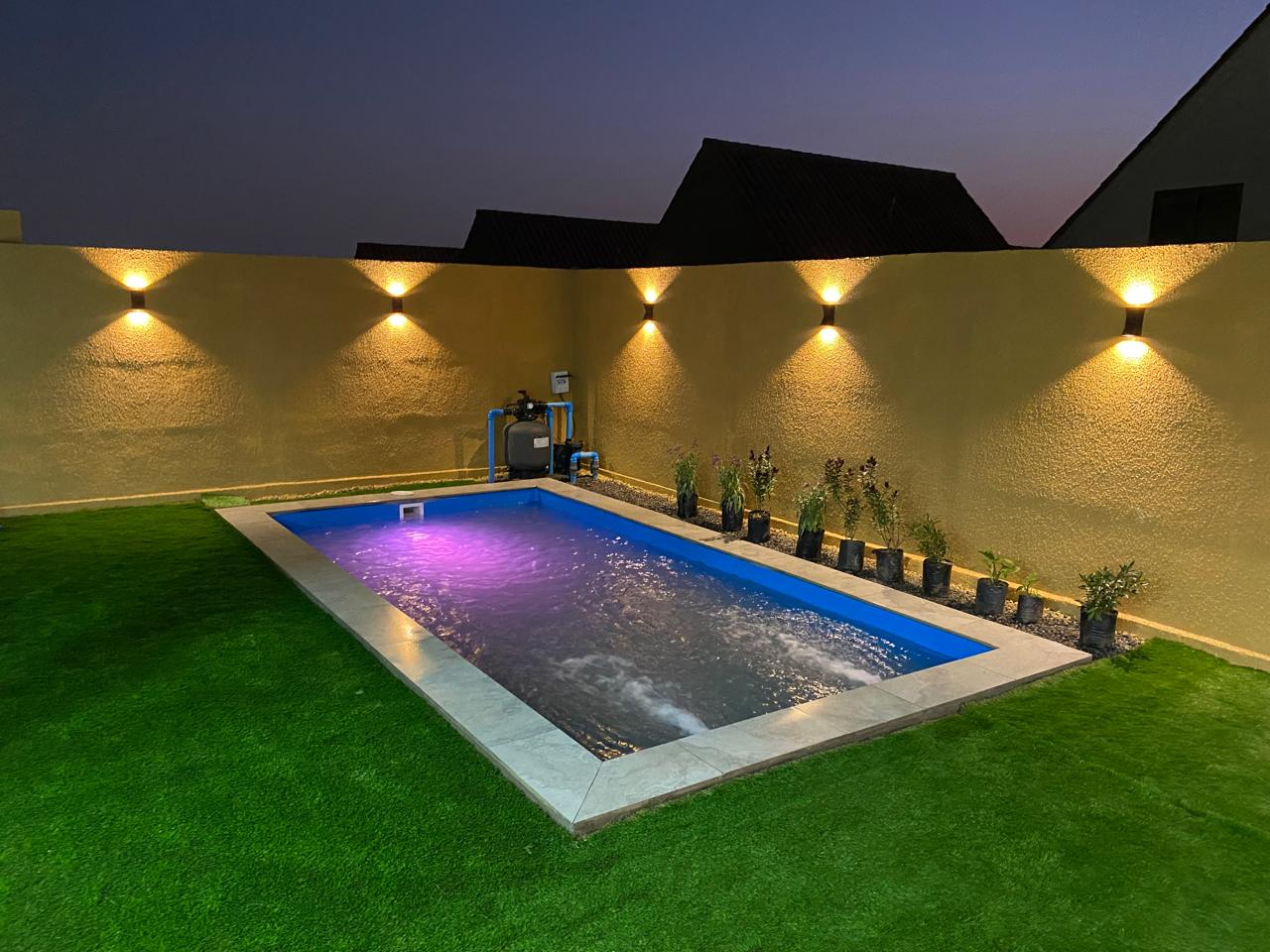 Piscina iluminada al anochecer con apliques de luz cálida